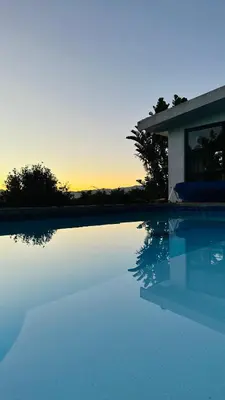 a swimming pool with the sun setting behind a house at Kleine Villa mit Pool und freie Sicht auf die Berge in Somerset West