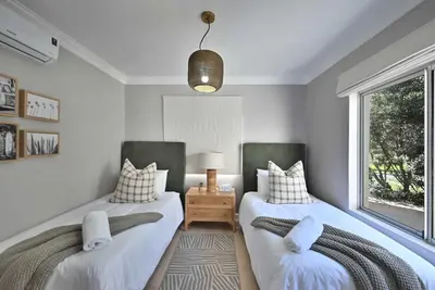 two twin beds in a room with a window at 3 Bedroom Cabana on the Beach in Cape Town