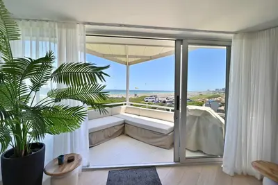a room with a balcony with a couch and a window at 3 Bedroom Cabana on the Beach in Cape Town