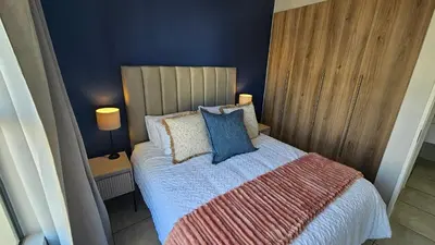 a bedroom with a bed with blue walls and two lamps at Luxury Apartment in Somerset West in Strand