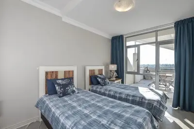 two beds in a room with a large window at Modern 2 Bedroom Apartment At Dolphin Beach in Cape Town