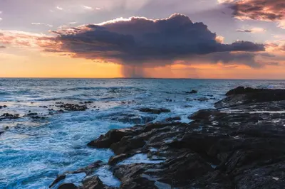 a storm cloud over the ocean with rocks at Modern 2 Bedroom Apartment At Dolphin Beach in Cape Town