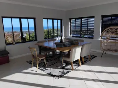a dining room with a table and chairs and windows at Chanteclair Holiday Home in Hermanus