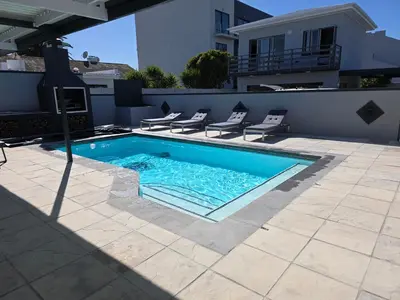 a swimming pool with chairs and a house at Dolphin Paradise in Cape Town