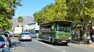a green bus driving down a city street with cars at Le Franschhoek Hotel & Spa by Dream Resorts in Franschhoek
