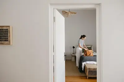 a woman is standing on a bed with a bag at Dorpshuis Apartment, Main Street, Paarl in Paarl