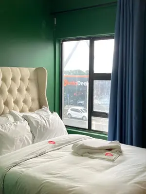 a bed with white sheets and a window with a car outside at Pro Max Guesthouse Goodwood in Goodwood