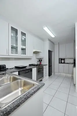a kitchen with white cabinets and a stainless steel sink at Townhouse in Bloubergstrand in Cape Town