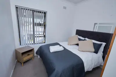a bedroom with a bed with a blue blanket and a window at Townhouse in Bloubergstrand in Cape Town