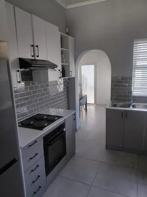 a kitchen with white cabinets and a stove top oven at Rihla Residences - Hanbury Road in Cape Town