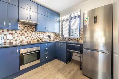 a kitchen with blue cabinets and a stainless steel refrigerator at Portifino on lake 221 The Island Club in Cape Town
