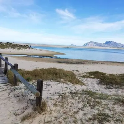 a beach with a fence and a body of water at Die Steenbras in Fisherhaven
