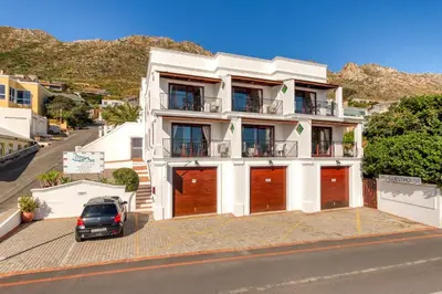 a white building with a car parked in front of it at Berg en Zee Guesthouse in Gordonʼs Bay