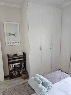 a bedroom with white cabinets and a bed with towels at Torbrae Cottage in Hermanus