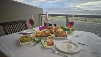 a table with a plate of food and two glasses of wine at Seaspray Apartment Blauberg in Cape Town