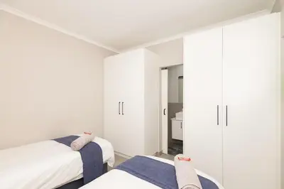 a white bedroom with two beds and white cabinets at Durbanville Daydream in Durbanville