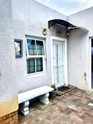 a white house with a bench in front of a door at Ebgow Cottage in Cape Town