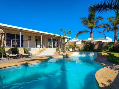 a swimming pool in front of a house with palm trees at Hajo's Lodge & Spa in Cape Town