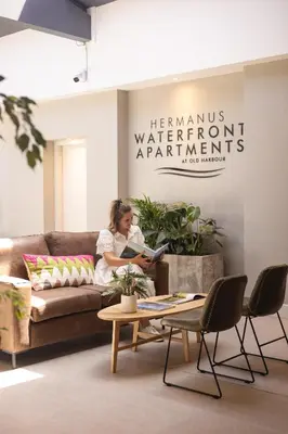 a woman sitting on a couch reading a book at Oceanfront Duplex Apartments, Hermanus Waterfront in Hermanus