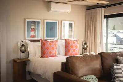 a bedroom with a bed and a couch and a window at Oceanfront Duplex Apartments, Hermanus Waterfront in Hermanus