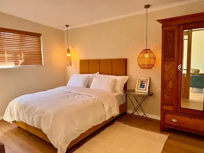 a bedroom with a bed and a table and a window at Mimosa Cottage in Cape Town