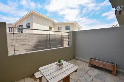 a balcony with a wooden table and a bench at 3B Sandy Bay in Cape Town