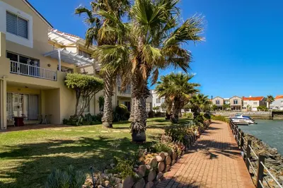 a house with palm trees next to a canal at Sunny Apartment Harbour Island in Gordonʼs Bay