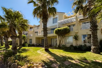 an apartment building with palm trees in front of it at Sunny Apartment Harbour Island in Gordonʼs Bay