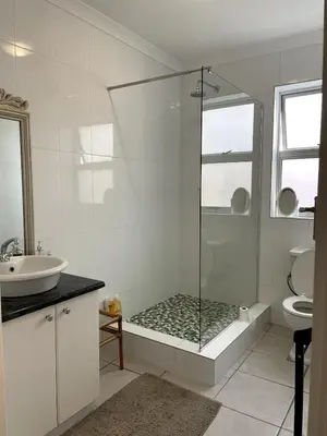 a white bathroom with a shower and a sink at Secret Coastal Garden in Hermanus