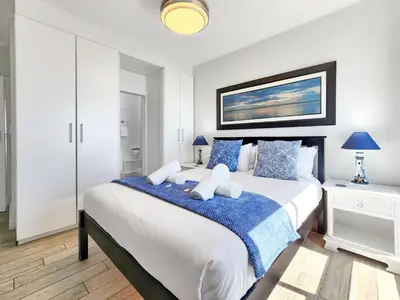 a bedroom with a large bed with blue and white pillows at Neptune Isle Oceanfront 3-Bed with Pool in Cape Town