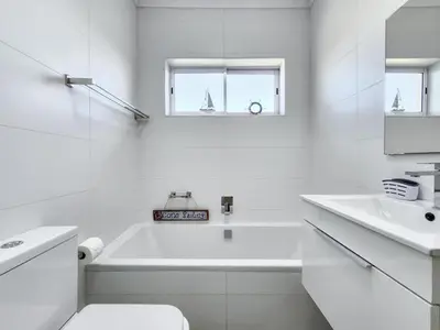 a white bathroom with a tub and a sink at Neptune Isle Oceanfront 3-Bed with Pool in Cape Town