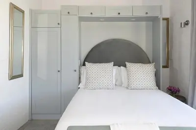 a bedroom with a white bed with a large headboard at The Little Vineyard Cottage in Franschhoek
