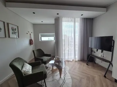 a living room with two chairs and a flat screen tv at Trendy Studio Apartment in On Park in Cape Town