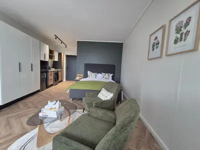 a living room with a bed and a couch and chairs at Trendy Studio Apartment in On Park in Cape Town
