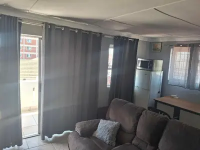 a living room with a brown couch and a kitchen at White house apartment in Cape Town