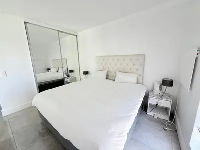 a white bedroom with a large bed and a mirror at Italian luxe 6 sleeper apartment near canal walk in Cape Town