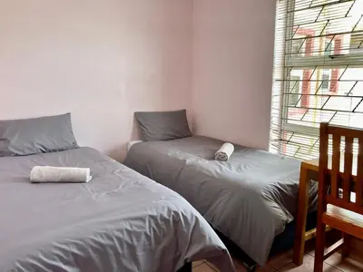 two beds in a small room with a window at Unit 1 GatherPoint Sleeps 6 Self-Catering Group in Belhar, Cape Town in Belhar