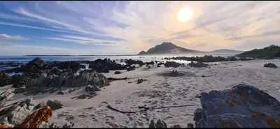 a beach with rocks and the sun in the sky at The Barracks at Brigadoon Village in Bettyʼs Bay
