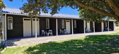 a black house with chairs and tables in front of it at The Barracks at Brigadoon Village in Bettyʼs Bay