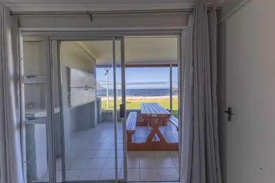 a door to a balcony with a table and a view of the ocean at Fleurpark 6 in Gordonʼs Bay