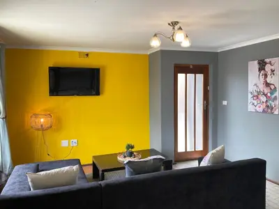 a living room with a couch and a yellow wall at Unit 1, TraversHub Sleeps 6 Self-Catering Group Belhar, CT in Belhar