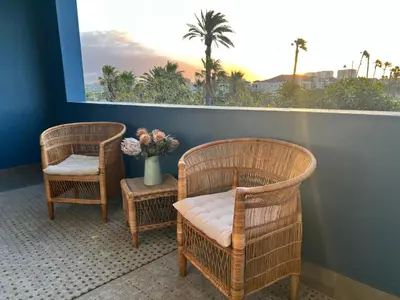 two wicker chairs and a vase with flowers on a balcony at Divine Apartment Century City in Cape Town