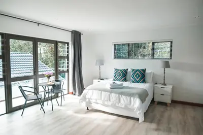 a white bedroom with a bed and a table and chairs at Crayfish at Hermanus Reefs in Hermanus