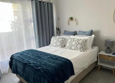 a bedroom with a bed with a blue blanket on it at Rissie's 3 Bedroom Apartment in Gordonʼs Bay