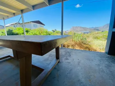 a wooden table on a porch with a view of a field at Fynbossie in Pringle Bay