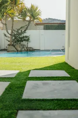 a garden with grass and stepping stones and palm trees at Beach House in Sunset Beach in Cape Town