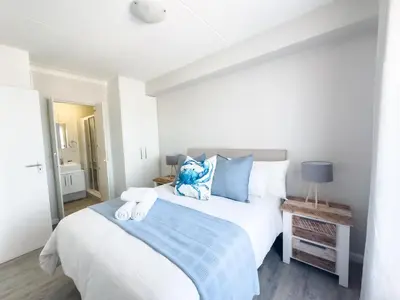 a bedroom with a large white bed with blue pillows at Manchester Heights Deluxe Apartments in Cape Town