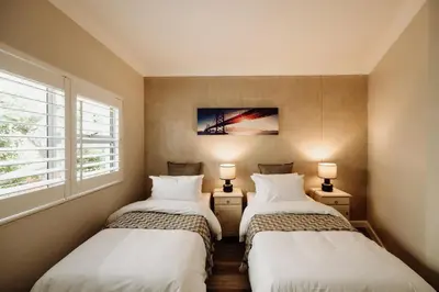 two beds in a room with two lamps and a window at Coats Haven in Hermanus