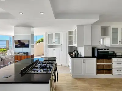 a kitchen with white cabinets and a black counter top at Seaside Serenity with Ocean View in Cape Town