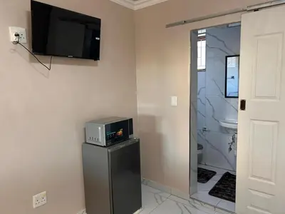 a room with a television on a wall with a refrigerator at New Dawn Guest House in Goodwood